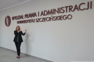 Otwarcie budynku Wydziału Prawa i Administracji Uniwersytetu Szczecińskiego. W tle biała ściana z dużym bordowym napisem Wydział Prawa i Administracji Uniwersytetu Szczecińskiego. Z przodu dziekan Wydziału dr hab. Ewelina Cała-Wacinkiewicz, prof. US wskazująca palcami na napis.