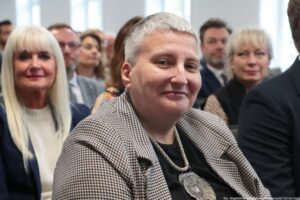 Otwarcie budynku Wydziału Prawa i Administracji Uniwersytetu Szczecińskiego. Ujęcie bokiem na ludzi siedzących w rzędach w sali. Na pierwszym planie prorektor dr hab. Kinga Flaga-Gieruszyńska, prof. US.