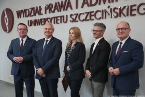 Otwarcie budynku Wydziału Prawa i Administracji Uniwersytetu Szczecińskiego. W tle biała ściana z dużym bordowym napisem Wydział Prawa i Administracji Uniwersytetu Szczecińskiego. Do zdjęcia pozują przedstawiciele władz miejskich, konserwator zabytków, rektor US i dziekan WPiA.