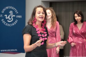 Otwarcie budynku Wydziału Prawa i Administracji Uniwersytetu Szczecińskiego. Na pierwszym planie dyrygentka (ujęcie do pasa). W tle Chór Uniwersytetu Szczecińskiego – kobiety ubrane w ciemnoróżowe suknie.