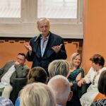 zdjęcie przedstawiające stojącego wypowiadającego się mężczyznę, oraz część wsłuchanej publiczności