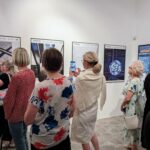 zdjęcie przedstawiające ludzi oglądających wywieszoną na ścianach wystawę