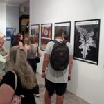 zdjęcie przedstawiające ludzi oglądających wywieszoną na ścianach wystawę