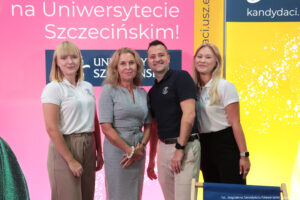 Troje pracowników Biura Rekrutacji (dwie kobiety i jeden mężczyzna) w polówkach z logiem Uniwersytetu Szczecińskiego stoją razem z prorektor ds. studenckich dr hab. Katarzyna Kotarska, prof. US (druga od lewej) na tle różowej ścianki z napisem: Zabłyśnij na Uniwersytecie Szczecińskim. Słowa „zabłyśnij” poza kadrem.