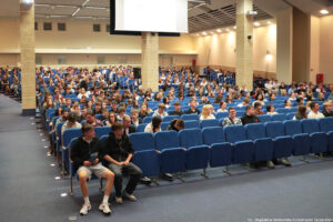 Ujęcie bokiem na siedzenia w auli uniwersyteckiej podczas wydarzenia Szczeciński Salon Maturzystów – Perspektywy 2025. Niebieskie fotele zajęte przez przyszłorocznych maturzystów.