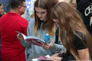 Dwie uczennice czytające informatory podczas Szczecińskiego Salonu Maturzystów – jedna przodem, druga bokiem. W tle inni uczestnicy wydarzenia.