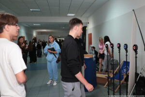 Uczestnik Szczecińskiego Salonu Maturzystów. W tle leżak z logiem Uniwersytetu Szczecińskiego i inni uczestnicy.