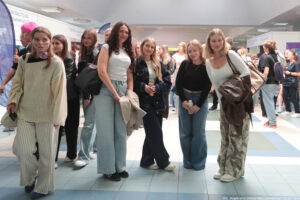 Pozujące do zdjęcia na korytarzu cztery uśmiechnięte uczennice w tłumie uczestników Szczecińskiego Salonu Maturzystów. Po lewej i po prawej stoiska uczelni z całej Polski.