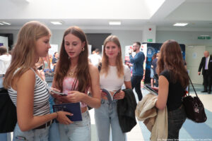 Cztery uczennice trzymające informatory na korytarzu podczas Szczecińskiego Salonu Maturzystów. Dziewczyna po prawej stoi tyłem. W tle stoiska uczelni z całej Polski i wejście do auli uniwersyteckiej.