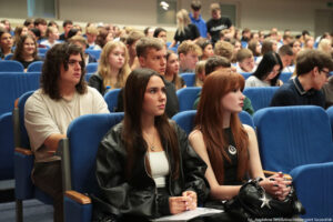 Ujęcie bokiem na siedzenia w auli uniwersyteckiej podczas wydarzenia Szczeciński Salon Maturzystów – Perspektywy 2025. Niebieskie fotele zajęte przez przyszłorocznych maturzystów.