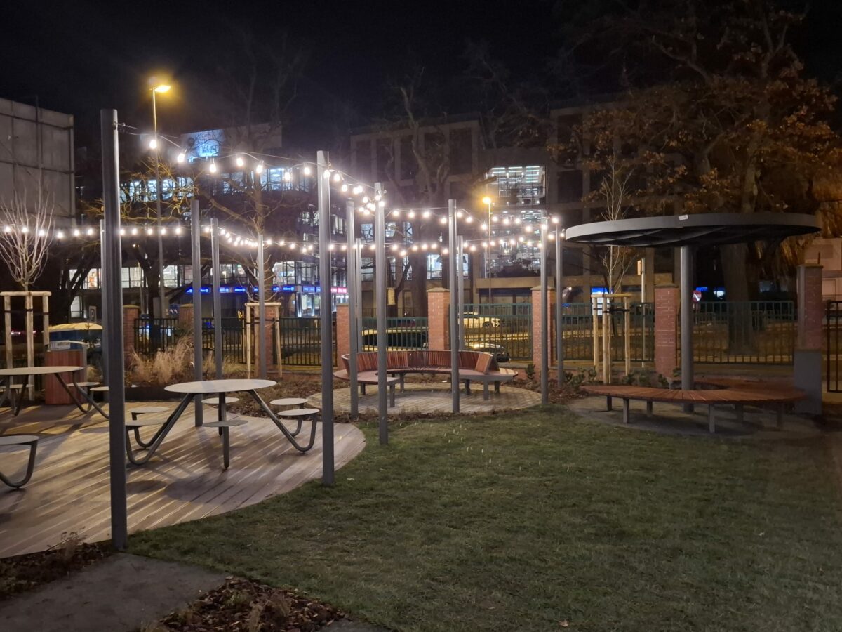 Ujęcie nocą na Piastów Chill Garden, czyli strefę relaksu, która powstała na terenie Uniwersytetu Szczecińskiego. Na zdjęciu ławki z krzesłami, nasadzenia i zawieszone u góry świecące lampki.