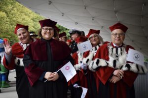 Troje prorektorów Uniwersytetu Szczecińskiego ubranych w czerwone togi z gronostajami – dwie kobiety i mężczyzna trzymający białą flagę z granatowym logiem US (z prawej). Druga od lewej przedstawicielka Zachodniopomorskiej Szkoły Biznesu w czarno-bordowej todze trzymająca flagę z logiem swojej uczelni.