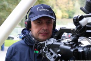 Zbliżenie na operatora kamery, który na głowie ma słuchawki i granatową czapkę z białym logiem Uniwizji – Telewizji Uniwersytetu Szczecińskiego.