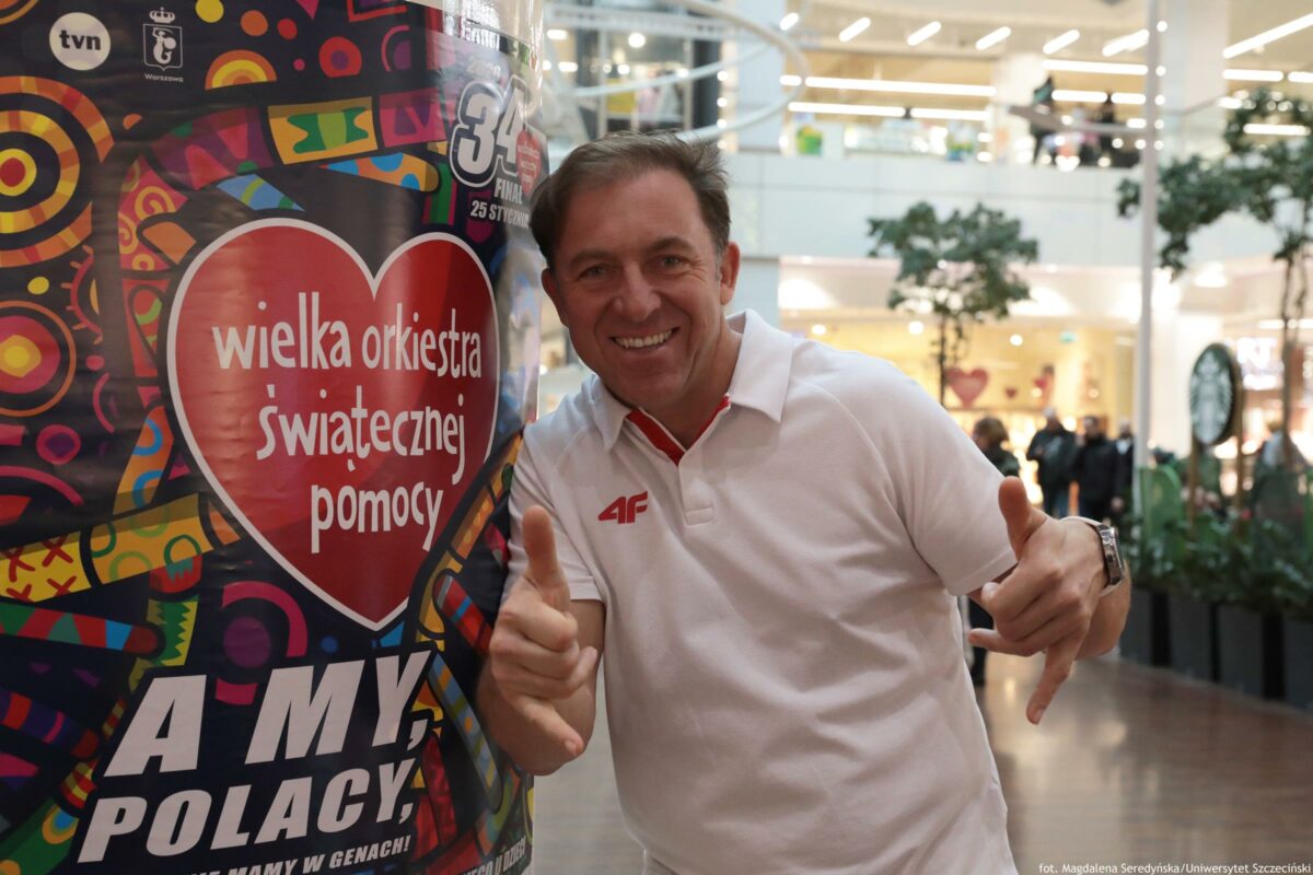 Mistrz olimpijski w wioślarstwie – Marek Kolbowicz – pozuje do zdjęcia przy plakacie Wielkiej Orkiestry Świątecznej Pomocy.