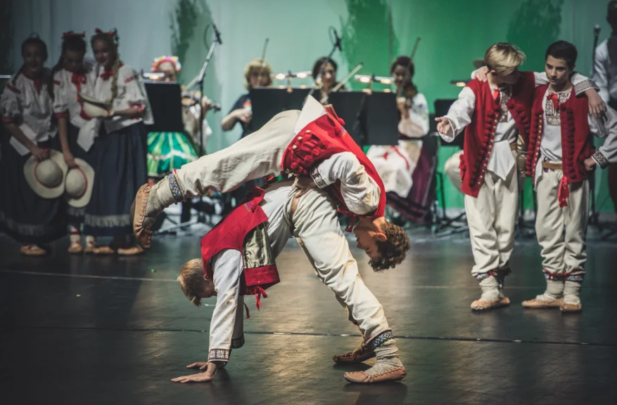 grupa muzyków na tylnym planie fotografii oraz tancerze tańca ludowego na froncie