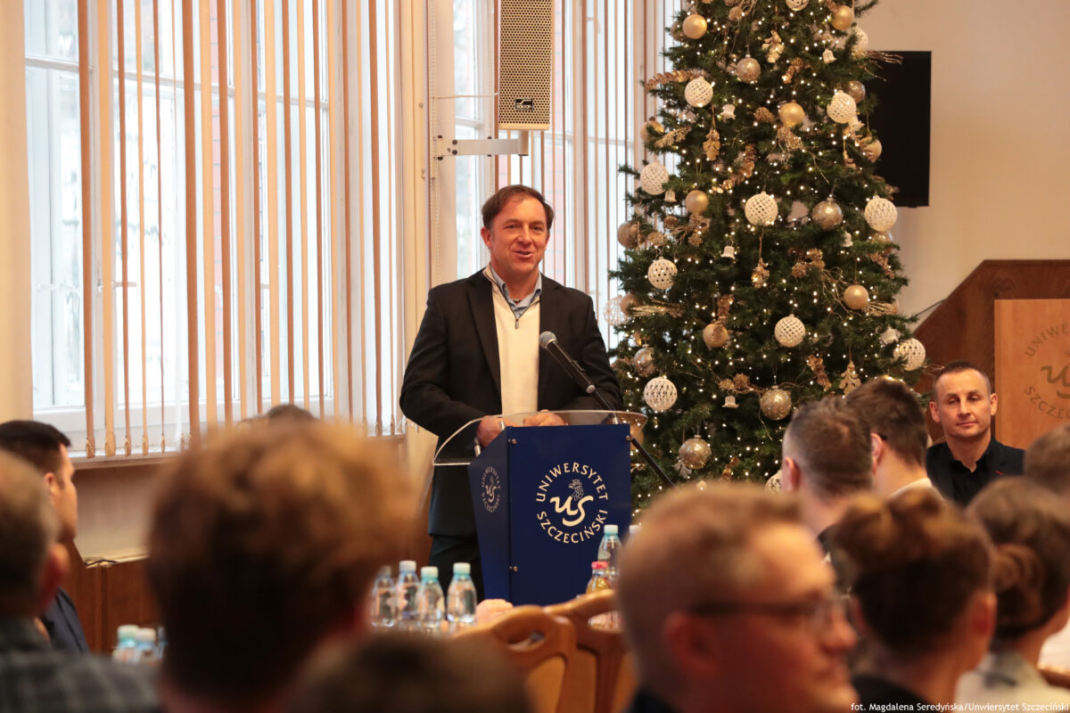 zdjęcie grupy ludzi siędzących w sali senatu podczas spotkania, jeden z mężczyzn stojący przy mównicy