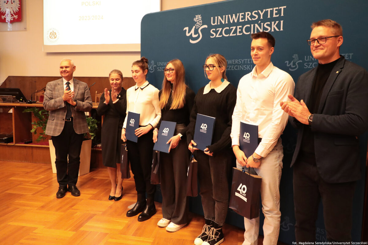 zdjęcie przedstawiające grupę ludzi pozujących na ściance US z teczkami