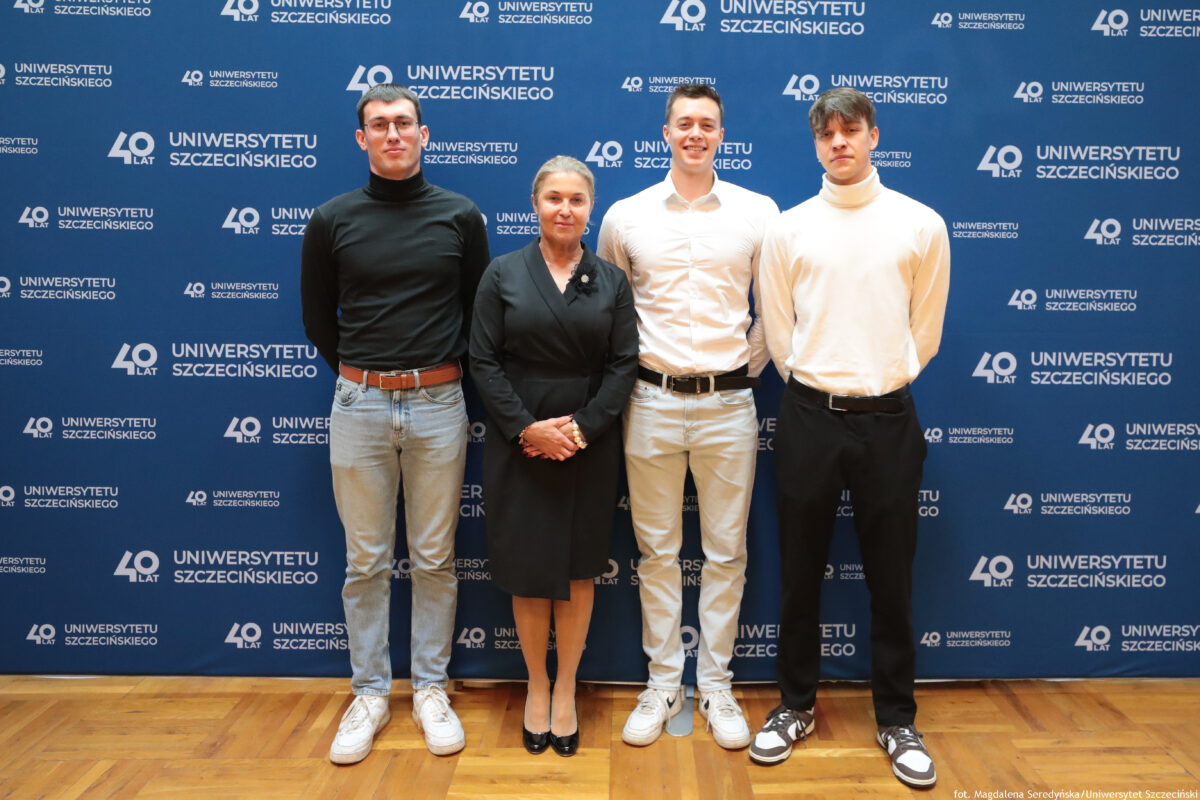 zdjęcie przedstawiające troje mężczyzn oraz jedną kobietę pozujących na ściance US