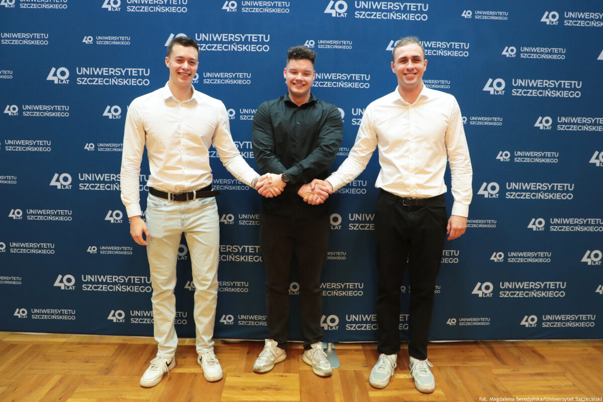 zdjęcie przedstawiające 3 mężczyzn pozujących na ściance US