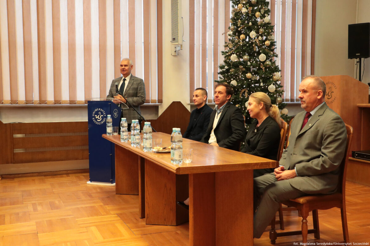 zdjęcie przedstawiające czworo osób siedzących przy stole prezydialnym oraz wypowiadającego się przy mównicy mężczyznę