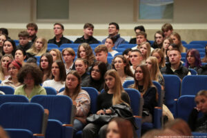 Ujęcie bokiem. Aula. Na niebieskich fotelach siedzi kilkudziesięcioosobowa grupa studentów – uczestników Dni Adaptacyjnych.