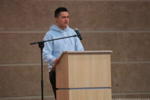 Aula. Podest z mównicą, za którym stoi przedstawiciel Uniwersytetu Szczecińskiego. Po lewej mikrofon na statywie.