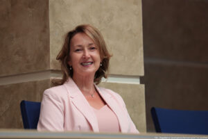 Aula. Za biurkiem siedzi uśmiechnięta przedstawicielka uczelni wprowadzająca studentów w Dni Adaptacyjne.