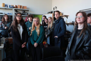 Pokój montażowy. Dookoła metalowe półki ze sprzętem typu, kamery, kable, skrzynki. Na pierwszym planie kilkunastoosobowa grupa studentów – uczestników Dni Adaptacyjnych.