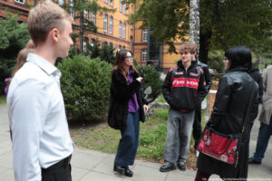 Na pierwszym planie kilkoro uczestników Dni Adaptacyjnych. W tle krzaki, drzewa i zabytkowy budynek z cegły.