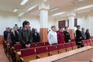 Sala wykładowa (ujęcie bokiem). Przed bordowymi krzesłami stoją studenci – uczestnicy Dni Adaptacyjnych.