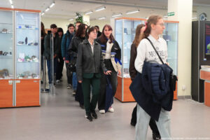 Kilkunastoosobowa grupa studentów wchodzi do Muzeum Geologicznego Uniwersytetu Szczecińskiego. Mijają ustawione po bokach dwie wysokie przeszklone gabloty z eksponatami.