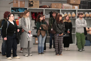 Kilkunastoosobowa grupa studentów w Rescue LAB – miejscu, w którym każdy może nauczyć się udzielania pierwszej pomocy. W tle na regałach sprzęt: fantomy, kamizelki.