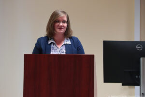 Sala wykładowa. Za mównicą prodziekan do spraw studenckich Wydziału Humanistycznego – dr Agnieszka Szlachta. Po prawej czarny monitor.