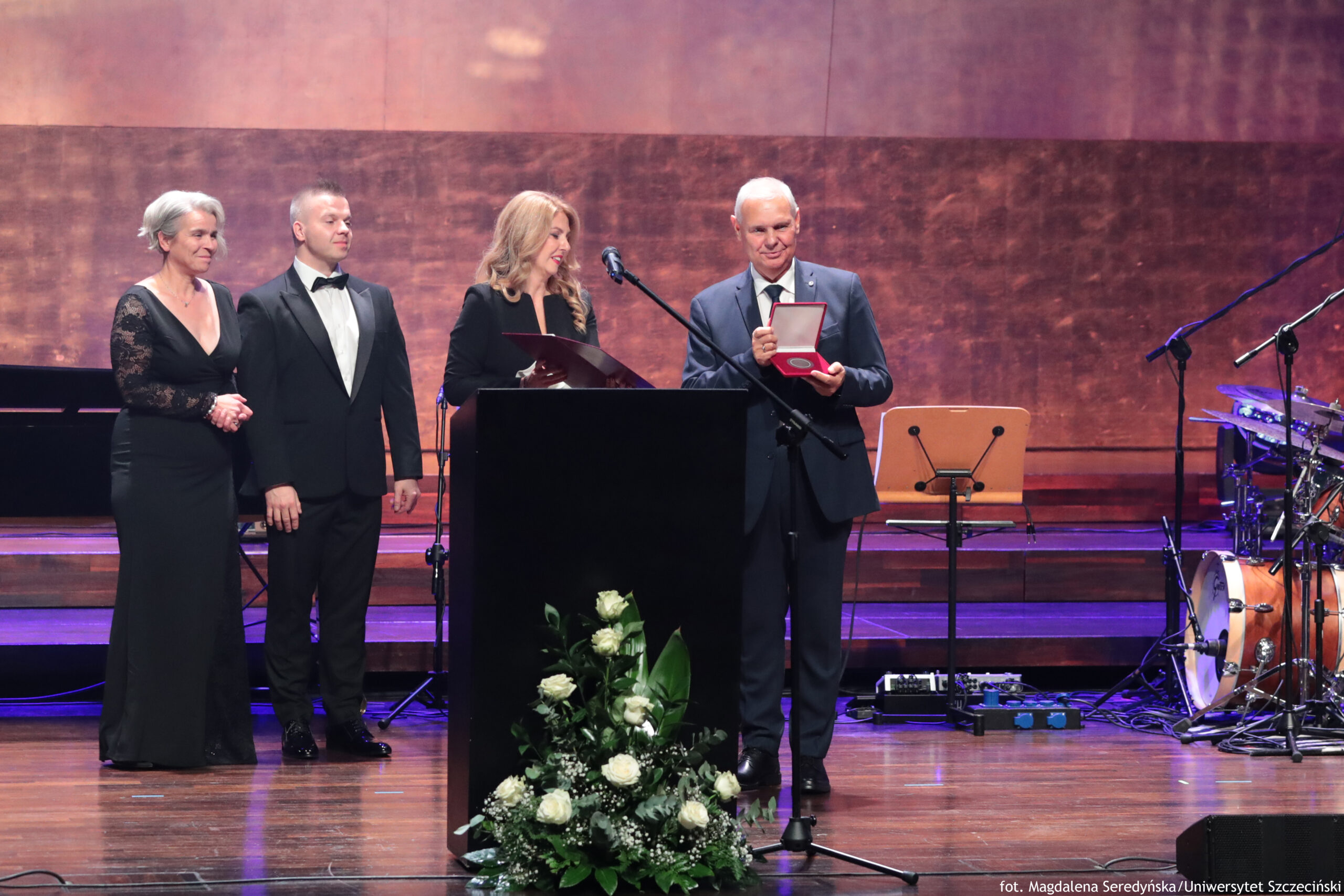 Gala 40-lecia Wydziału Prawa i Administracji Uniwersytetu Szczecińskiego. Scena. Na środku czarna mównica, a za nią dziekan Wydziału – dr hab. Ewelina Cała-Wacinkiewicz, prof. US. Obok po prawej rektor US – prof. dr hab. Waldemar Tarczyński trzymający medal w czerwonym etui. W tle dwoje prodziekanów wydziału.