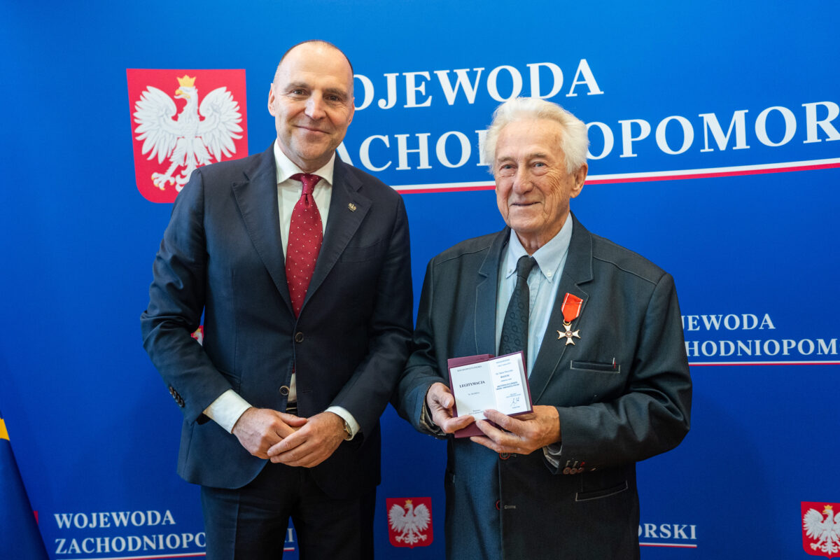 Wojewoda Zachodniopomorski – dr Adam Rudawski i prof. Tadeusz Białecki odznaczony Krzyżem Kawalerskim Orderu Odrodzenia Polski z odznaczeniem wpiętym w marynarkę. W tle niebieska ścianka z godłem Polski i białym napisem: Wojewoda Zachodniopomorski.