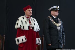 Inauguracja roku akademickiego. Scena. Czarne tło. Po lewej rektor Uniwersytetu Szczecińskiego ubrany w czerwoną togę z gronostajami. Po prawej rektor Akademii Morskiej ubrany w mundur.