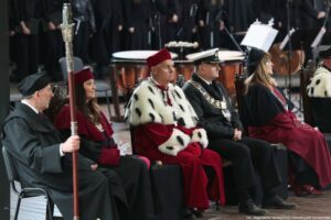 Scena. Inauguracja roku akademickiego. Ujęcie bokiem. Siedzący rektorzy szczecińskich uczelni – w środku rektor Uniwersytetu Szczecińskiego w todze z czerwonymi elementami i gronostajami. W tle bębny.