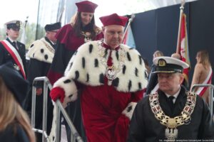 Ujęcie przodem. Inauguracja roku akademickiego. Schodzący ze sceny rektorzy szczecińskich uczelni – w środku rektor Uniwersytetu Szczecińskiego w todze z czerwonymi elementami i gronostajami. W tle pozostali uczestnicy wydarzenia.