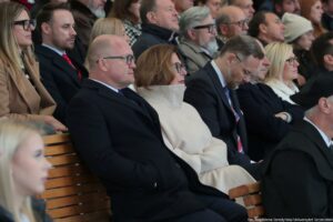 Ujęcie bokiem. Oficjele siedzą w rzędach podczas inauguracji roku akademickiego.