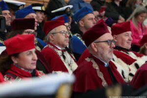 Ujęcie bokiem. Ubrani w czerwone togi z gronostajami prorektorzy Uniwersytetu Szczecińskiego oraz władze innych uczelni siedzą w rzędach podczas inauguracji roku akademickiego.