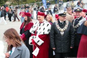Spacerek na uniwerek. Ujęcie bokiem. Na pierwszym planie rektorzy szczecińskich uczelni w uroczystych togach i mundurach. W tle inni uczestnicy wydarzenia.