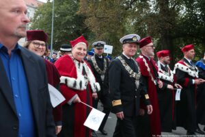 Spacerek na uniwerek. Ujęcie bokiem. Przedstawiciele szczecińskich uczelni ubrani w uroczyste togi z gronostajami. W tle drzewa.