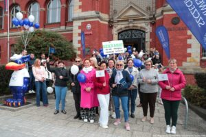 Spacerek na uniwerek. Przed zabytkowym gmachem rektoratu Uniwersytetu Szczecińskiego stoją ludzie z białymi i granatowymi balonikami. Po lewej duży posąg Gryfusia z logiem uczelni.