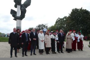 Spacerek na uniwerek. W pierwszym rzędzie oficjele. Za nimi przedstawiciele szczecińskich uczelni ubrani w uroczyste togi z gronostajami. W tle drzewa i pomnik Czynu Polaków (trzy orły).