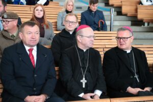 Inauguracja roku akademickiego. Widownia. Ujęcie na troje oficjeli z przodu (polityk i dwóch biskupów). W tle inni uczestnicy wydarzenia.