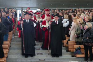 Inauguracja roku akademickiego. Schodzący po schodach przedstawiciele szczecińskich uczelni w uroczystych togach. Z przodu dwóch pedli w czarnych togach. Po bokach widownia Teatru Letniego.