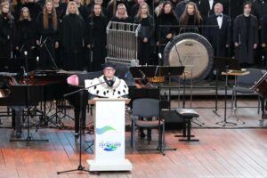 Inauguracja roku akademickiego. Za białą mównicą rektor Zachodniopomorskiego Uniwersytetu Technologicznego ubrany w czarną togę z gronostajami. Za nim instrumenty. W tle ubrany na czarno chór.