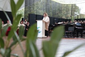 Inauguracja roku akademickiego. Scena. Wicemarszałkini Sejmu stojąca za białą mównicą. Przed nią mikrofon. W tle po prawej instrumenty i chór. Po lewej rektorzy szczecińskich uczelni w uroczystych togach. Na pierwszym planie nieostre liście.