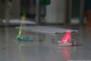 Noc Biologów 2026. Laboratorium. Na stole dwie szalki Petriego. Na tej po lewej zielony płomień, na tej po prawej różowy.