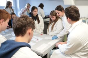Noc Biologów 2026. Laboratorium. Dziesięcioro nastoletnich uczniów w białych fartuchach przygotowuje się do przeprowadzenia eksperymentu.